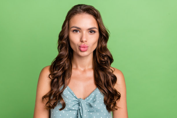 照片：年轻快乐的女人，眼神空灵，带着空气吻，心情愉悦，孤立在绿色背景上图片下载