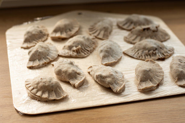 一张俯视角度拍摄的干净图片，展示了手工制作的传统饺子，边缘卷曲精美，整齐地摆放在白色的陶瓷盘中。图片下载