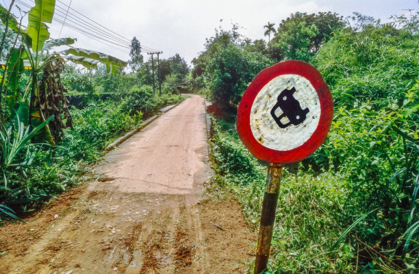 1994年3月23日，越南丛林中一条狭窄荒芜的乡村公路上，历史彩色照片，幽默地描绘了禁令标志上的一辆颠倒的汽车。图片下载