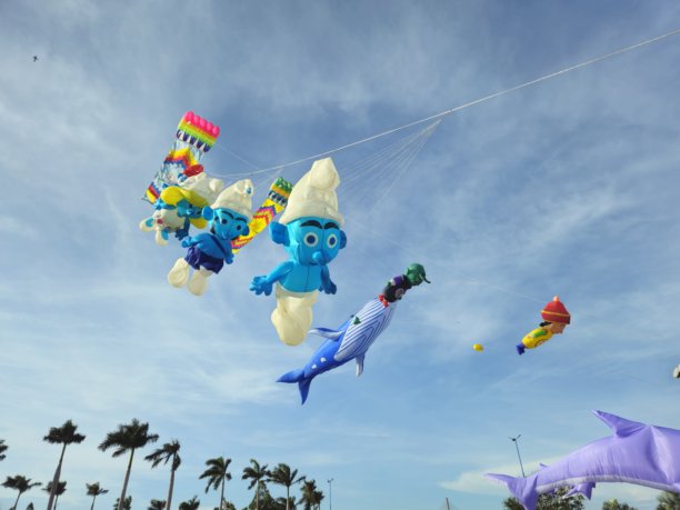 一群色彩鲜艳的风筝，有卡通人物造型的，也有长方形的，在晴朗的蓝天白云间飞舞。图片下载