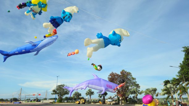 一群色彩鲜艳的风筝，形状有卡通人物和长方形，在越南芹苴市明亮的蓝天白云中飞翔。图片下载