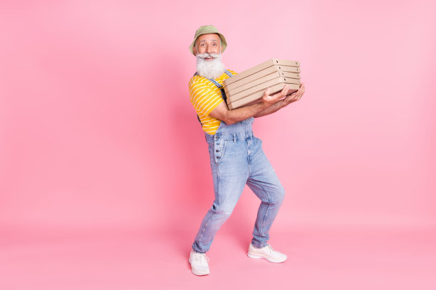 一名面带微笑的送货员抱着一摞披萨，订单量大，退休的快递员，在粉色背景下拍摄的全尺寸照片图片下载