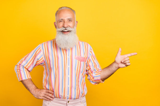 照片：穿着黄色衬衫的可爱成熟男子，微笑着指向黄色背景的空白空间图片下载