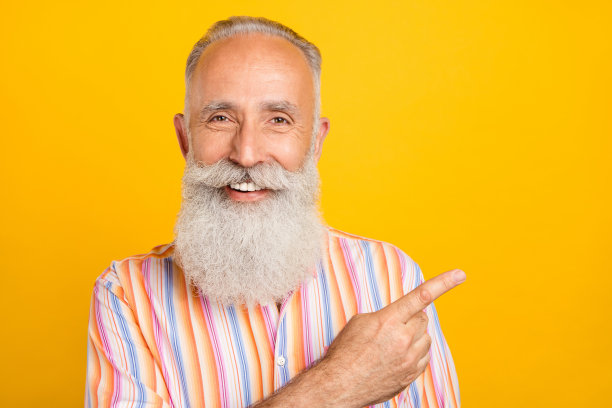 照片：一位穿着条纹衬衫的积极的年长顾问，手指着空旷空间，背景为黄色图片下载