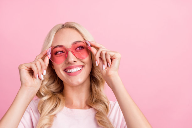 照片：一位戴着耳机、穿着T恤的千禧一代金色卷发女士，孤立在粉色背景上，欢呼雀跃图片下载