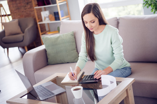 照片：一位可爱的年轻棕发女子独自在家，穿着蓝色衬衫坐在沙发上图片下载