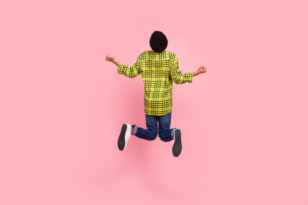 千禧一代的棕色头发的男人，穿着衬衫、牛仔裤和运动鞋，指向粉色背景上的空白空间，背景是全尺寸照片。图片下载