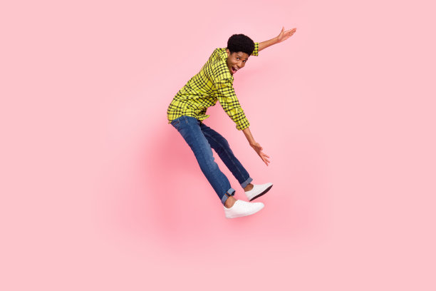 千禧一代棕发男子，穿着衬衫、牛仔裤和运动鞋，手指指向粉色背景上的空白处，全尺寸照片图片下载