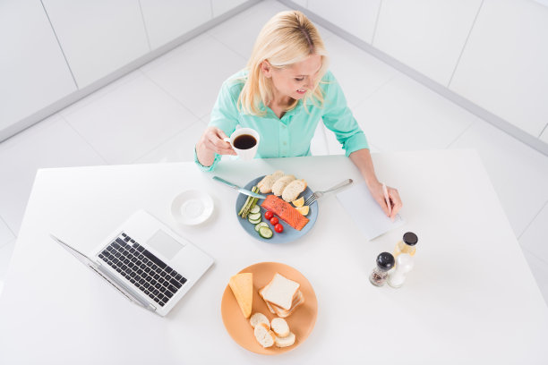 俯视角度拍摄的成熟快乐女厨师在厨房里穿着围裙做早餐的照片，室内拍摄。图片下载
