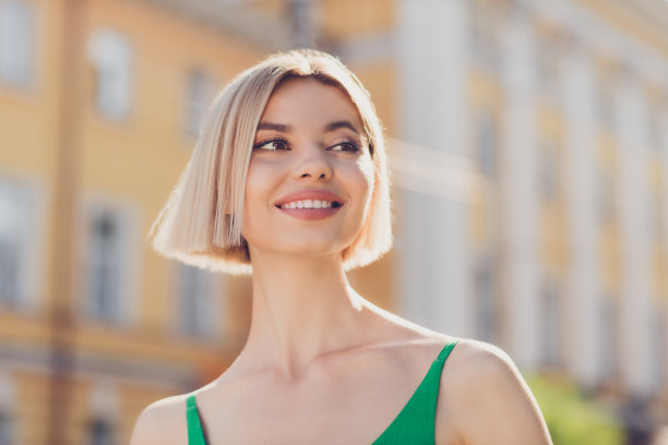 照片：可爱闪亮的年轻女士穿着绿色服装，挎着手提包，微笑着走在城市街道上，同时使用现代电子设备。图片下载