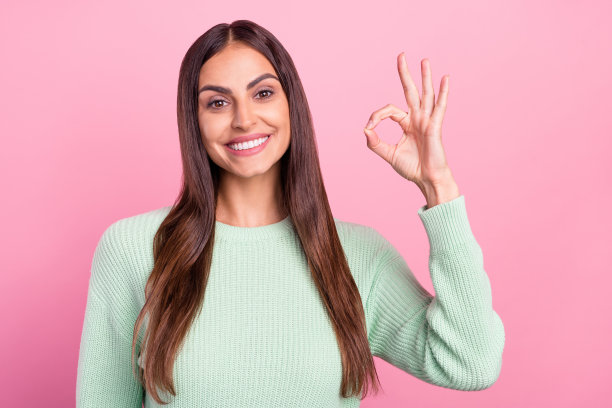 粉色背景上孤立的，穿着绿色套头衫的可爱千禧年棕发女士照片图片下载