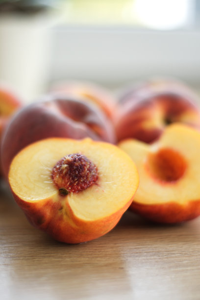 一张干净、简约的图片，展示了三颗成熟的桃子在木桌上呈对角线排列，具有浅景深和柔和的光线。图片下载