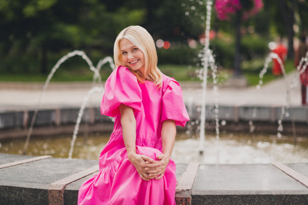 一位穿着粉色套装、面带笑容的可爱退休女士在城市街道上行走，照片风格图片下载