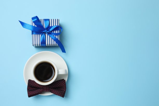 蓝色背景上礼物盒、丝带蝴蝶结、咖啡杯和领带的俯视照片图片下载