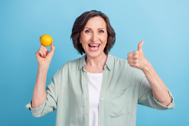 照片肖像：一位年长的女性，面带微笑，比出V字手势，在粉蓝色背景前，隔离拍摄。图片下载