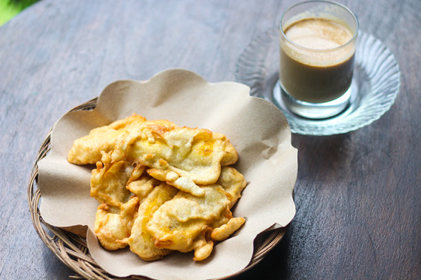 一张在质朴木桌上的热咖啡和炸香蕉（pisang goreng）的图片。图片下载
