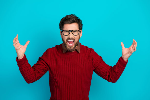 身穿红色毛衣、戴着眼镜的活力男子，双臂高举，在明亮的蓝色背景前大声呼喊，适合用于股票广告和生活方式图片图片下载