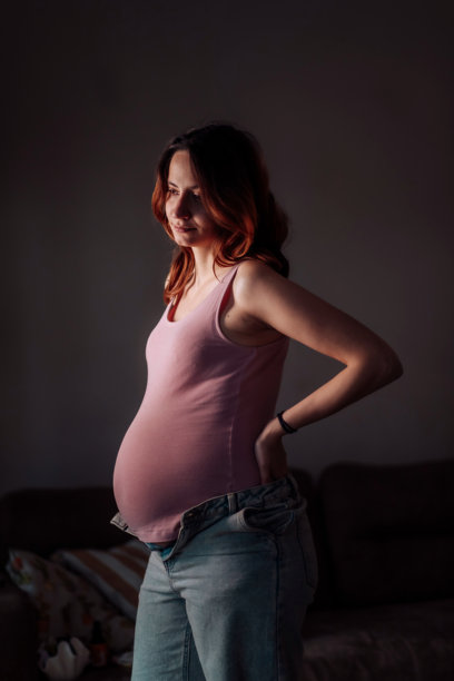穿着粉色背心和未扣牛仔裤的孕妇，若有所思地望向远方图片下载