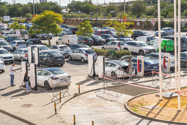 晴朗的天空下，拥挤的停车场里，几辆特斯拉电动汽车正在超级充电站充电。图片下载
