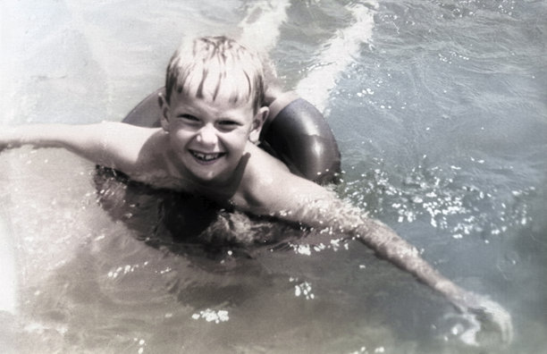 一个复古风格的肖像，描绘了一个可爱的金发男孩漂浮在海上的救生圈里。这是1971年的老照片。图片下载