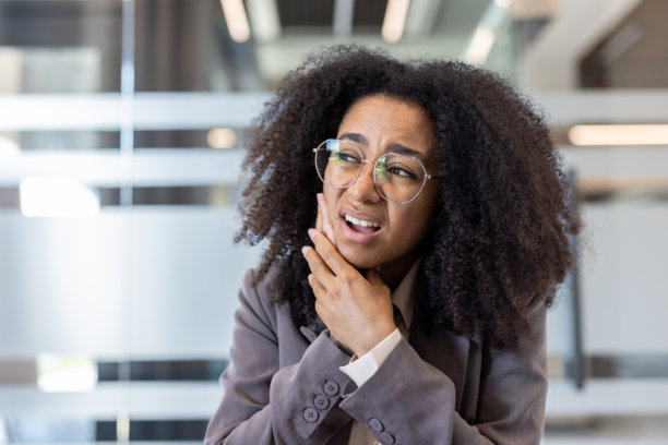 一位年轻的非裔美国女性在办公室，坐在书桌前，饱受牙痛折磨的特写照片图片下载