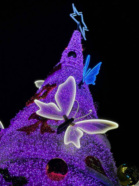 逼真的假针叶人造粉色云杉圣诞树，装饰着蝴蝶饰品和彩色饰球图片下载