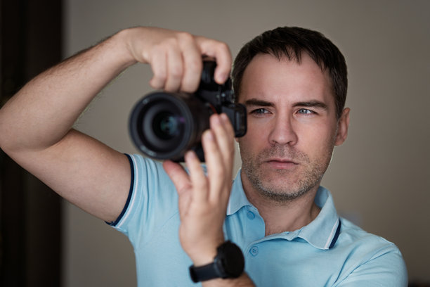 摄影师手持无反相机进行选择性对焦检查照片。狗仔队，摄影师通过相机观察拍摄对象。一位英俊的摄影师带着长焦镜头。图片下载