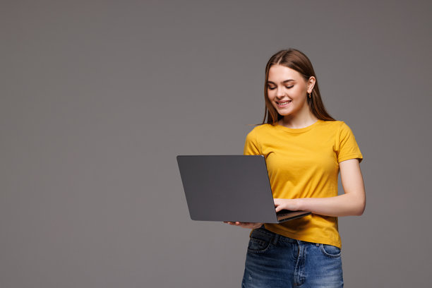 年轻女子在灰色墙壁背景前使用笔记本电脑摆姿势，照片隔离图片下载