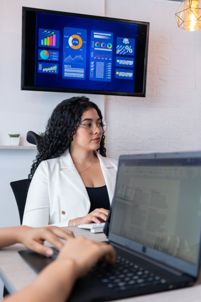 一位职业女性正在主持商务会议，数字屏幕上显示着图表和目标图片下载