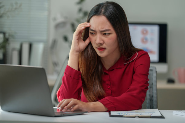 年轻的亚裔女商人长时间使用笔记本电脑工作，感到头痛和疲倦，她触摸着头，表情紧张地看着笔记本屏幕。图片下载
