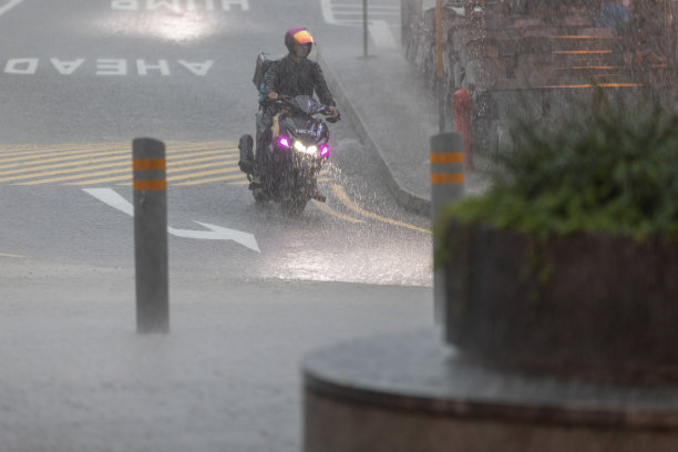 年轻男子在雨中街头骑摩托车。图片下载