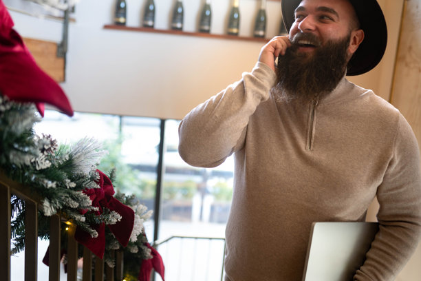 男人在咖啡馆远程工作，一手拿着手机打电话，一手处理多项任务图片下载