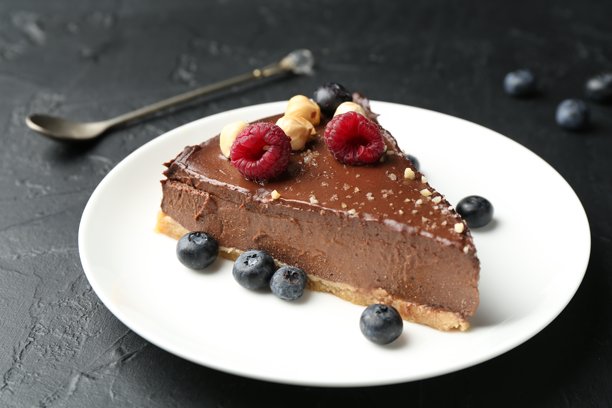 一块美味的巧克力芝士蛋糕，上面有坚果、浆果和勺子，放在黑色的桌子上，特写图片下载
