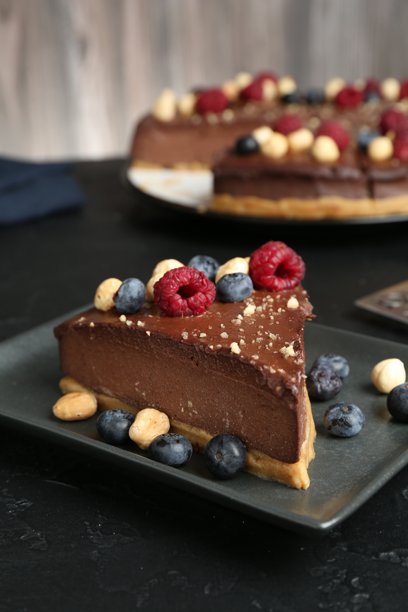 黑色桌上放着一块美味的巧克力芝士蛋糕，上面有坚果和浆果，特写图片下载