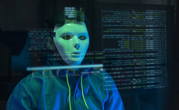 一个人戴着连帽衫和口罩，正在虚拟屏幕上操作笔记本电脑。黑客正在入侵公司系统。涉及网络安全和数据保护的概念。图片下载