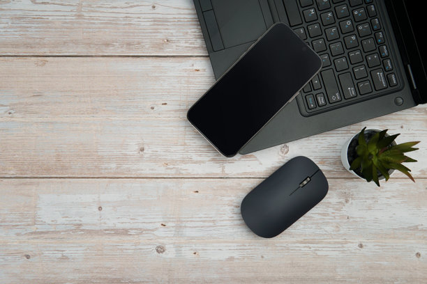 俯视角度的极简商务工作区，白色木桌上摆放着笔记本电脑、智能手机、鼠标和植物，代表着高效、数字化的工作环境和专业的办公室设置，并留有干净的复制空间。图片下载