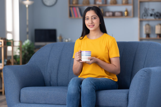 照片，穿着黄色T恤的可爱小女孩在家坐在沙发上图片下载