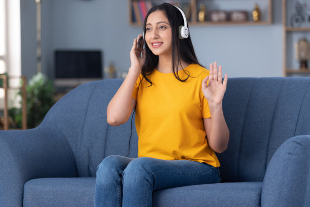 照片：一位戴着耳机、穿着黄色T恤的可爱年轻女老师，在家里的沙发上坐着图片下载