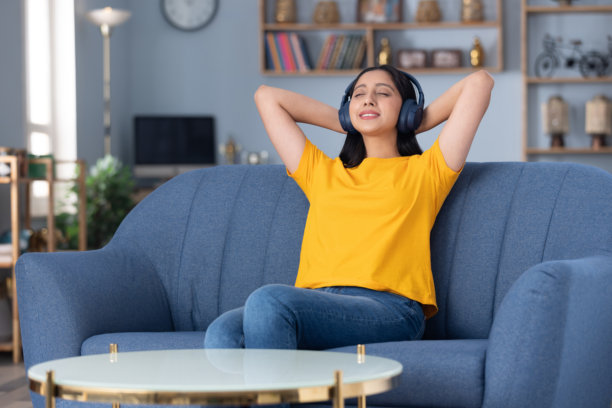 穿着黄色T恤的可爱小女孩在家中沙发上听音乐的库存照片图片下载