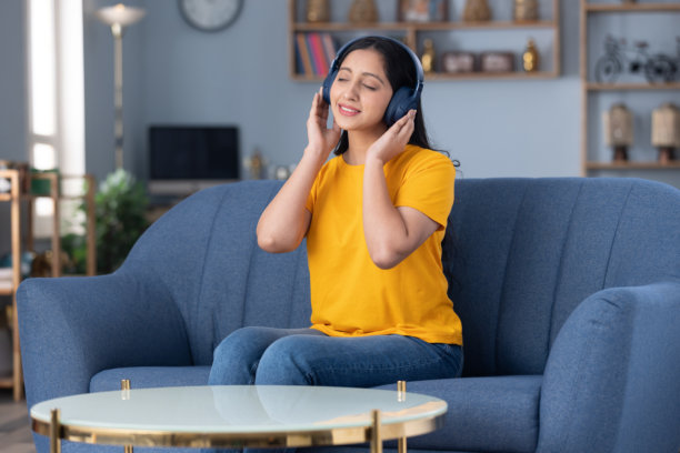 照片：穿着黄色T恤的可爱小女孩在家中沙发上坐着听音乐图片下载