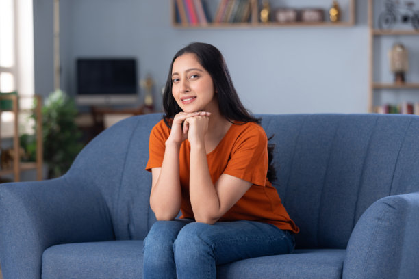 照片：一个穿着休闲服饰的美丽年轻女孩在家里的沙发上坐着图片下载