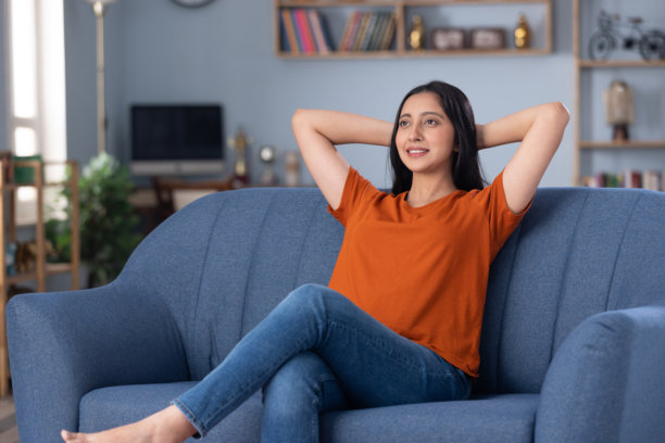 身穿休闲服饰的美丽年轻女孩在家中沙发上坐着的照片素材图片下载