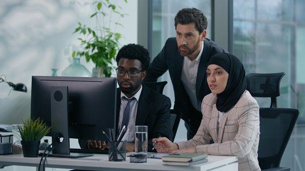 多元化的商务团队在办公室讨论项目营销策略，看向电脑屏幕，有非洲裔男性、戴头巾的女性和高加索男性，展现团队合作、会议和沟通。图片下载