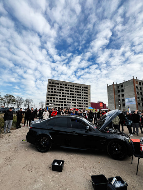 建筑工地上，人群围着一辆引擎盖敞开的时尚黑色宝马汽车图片下载