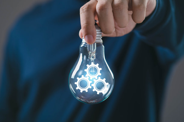 一只手握着透明的灯泡，里面有发光的齿轮图标，代表系统流程、自动化、工程工作流、用于业务运营的智能技术、生产力和创新管理。图片下载