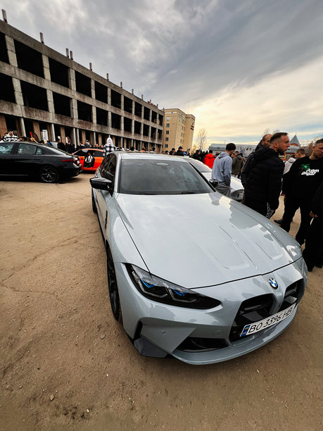 银色宝马 M3 G80 轿车停在一个拥挤的汽车展上，旁边是一栋未完工的建筑和建筑工地图片下载