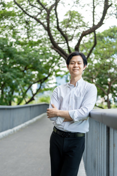 在公园户外，一位年轻的亚洲商界男士肖像。英俊有魅力的男性员工在绿色花园的办公室工作场所外自信地度过闲暇时光。图片下载