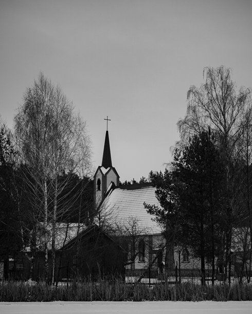 白雪覆盖、树木点缀的河岸上，一座教堂的黑白照片，河流已结冰。图片下载