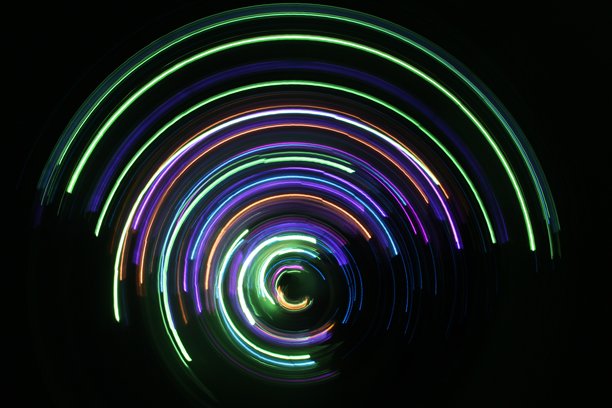 一张长时间曝光的照片。光绘摄影；鲜艳的彩色串灯以圆形漩涡图案在黑色背景上舞动图片下载