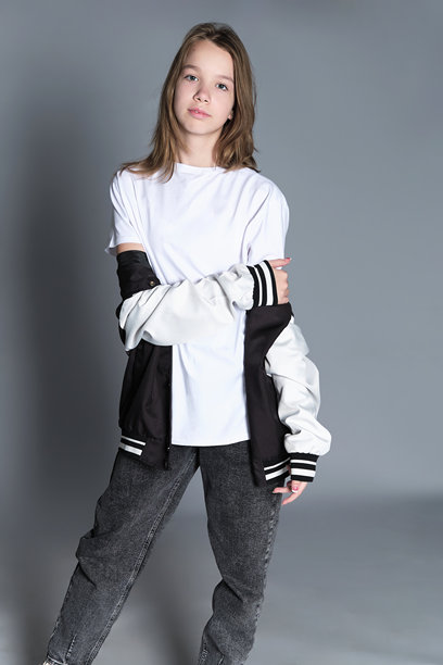 一位年轻女孩自信地整理头发，身穿休闲装外搭一件大学夹克。这张照片捕捉了青春和自我表达的精神，强调了当今现代世界的个性。图片下载